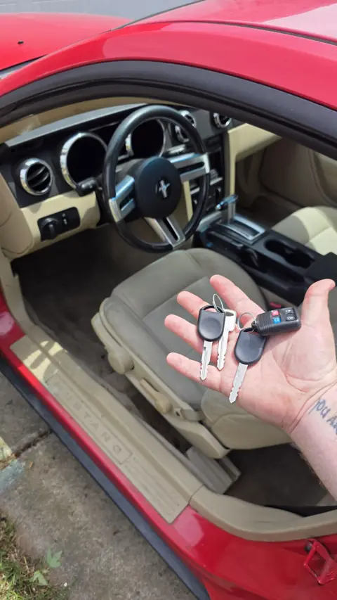 Two replacement Ford Mustang transponder keys and a remote made on site, held next to the open driver door