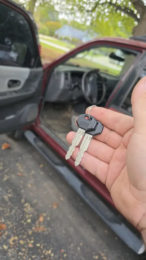 Two replacement keys made for a red SUV, held at the open driver door